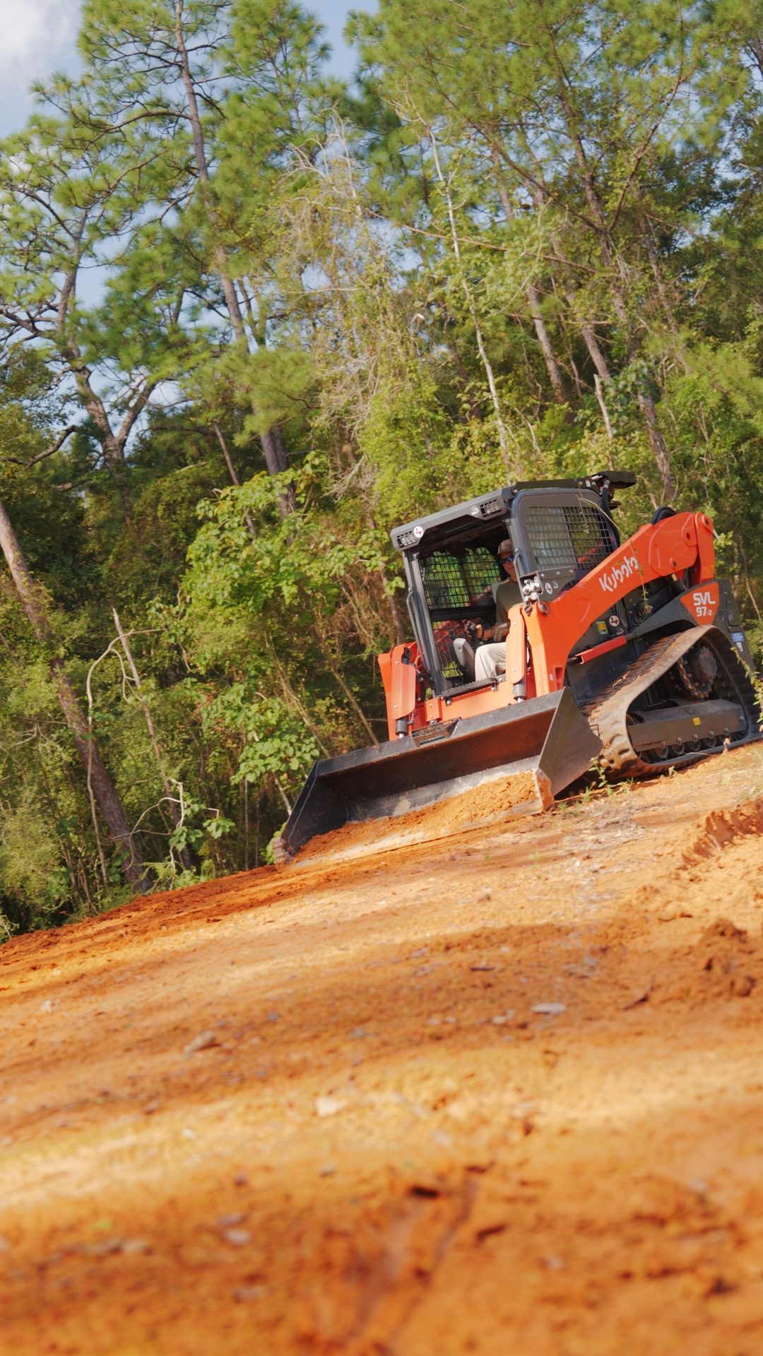 Tracked Kubota skid steer grading red dirt on a cleared site